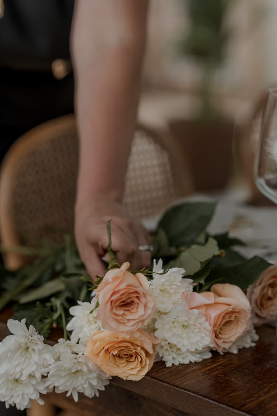 Peach roses and white chrysanthemums gathered along the edge of a wooden table before they are arranged