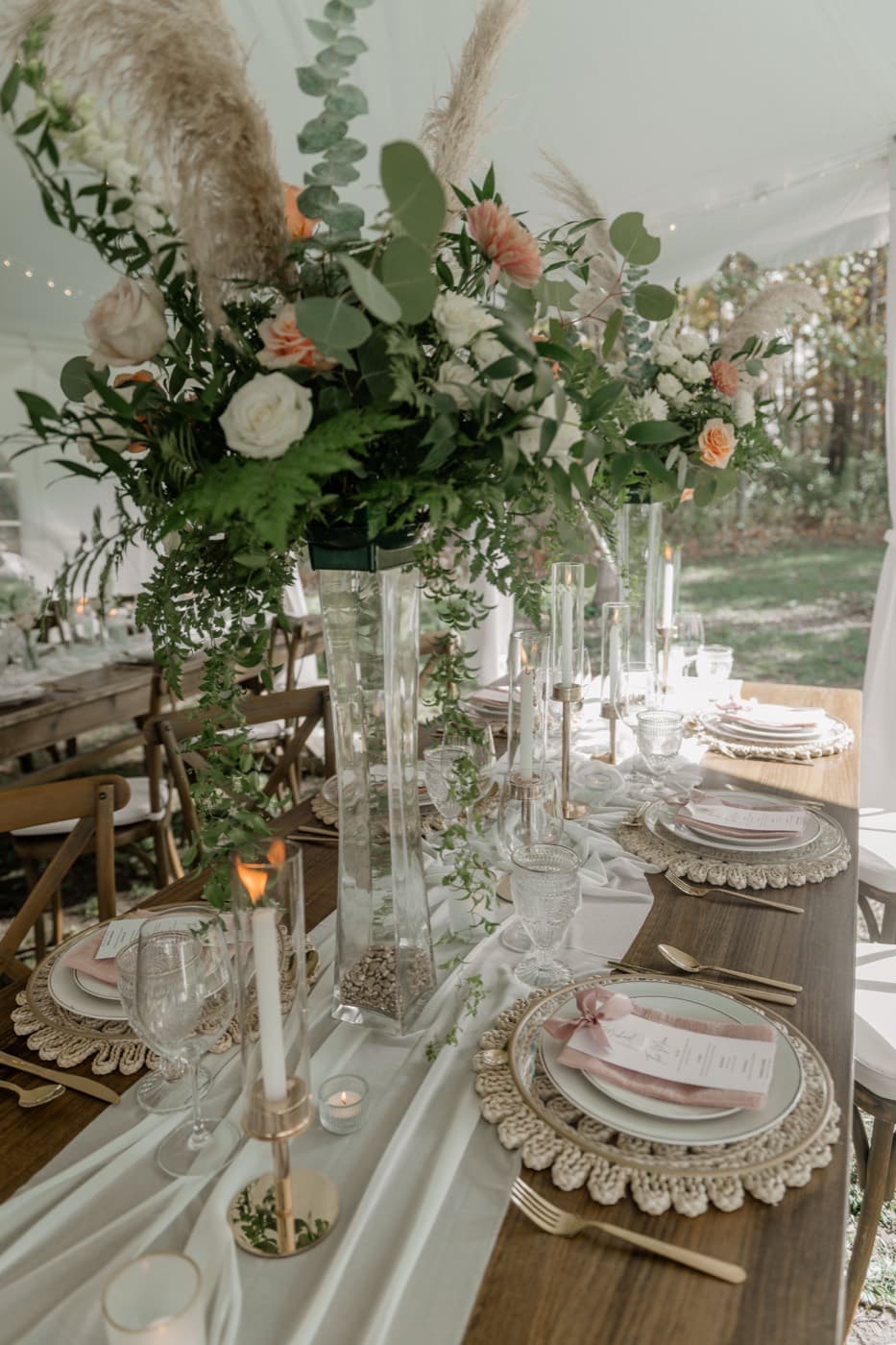 A tall centrepiece of pampas grass, eucalyptus and peach and white roses rising above the tented table