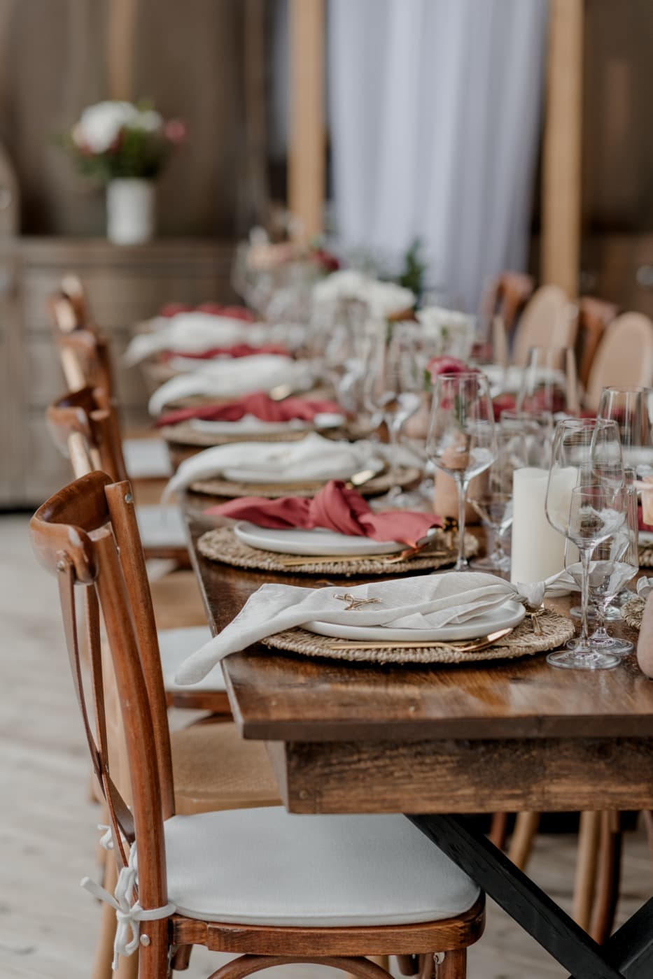 Place settings receding down the harvest table, cream and rust napkins on woven chargers with pillar candles between them