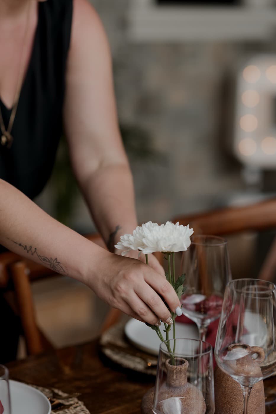 A hand settling a white chrysanthemum into a terracotta bud vase on the set table